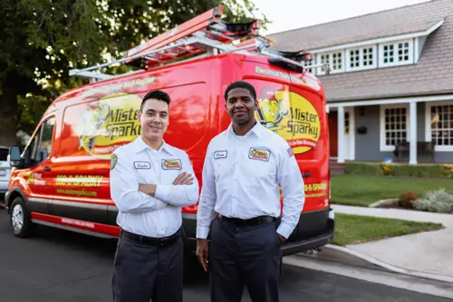 two electricians from mister sparky standing outside work truck and home